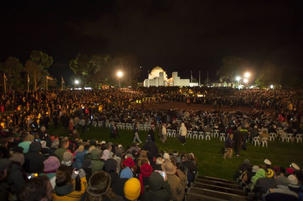 Large numbers of people both seated and standing around the Parade Ground and Stone of Remembrance in front of the Australian War Memorial.