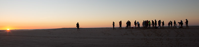 Silhouettes of people against an orange and salmon sky watching the sunset over the Gulf of Carpentaria.