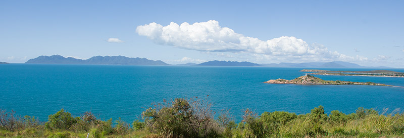 Turquoise blue sea beneath light blue sky and white fluffy cloud. Gloucester Island is on the skyline.